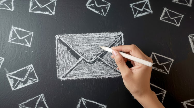 Writing and sending a lot of e-mail concept. Businessman drawing e-mail icons on chalkboard. hand holding a piece of white chalk, actively drawing a large, clean envelope on a dark