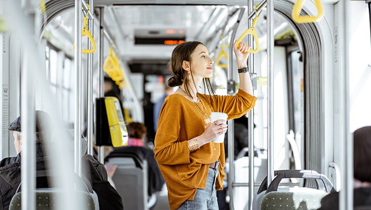Young woman passenger enjoying trip at the public transport, standing with coffee in the modern tram