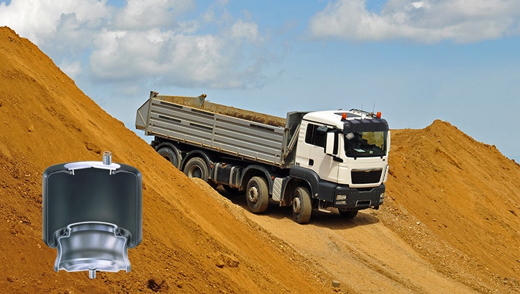A large white dump truck drives up a steep dirt incline under a partly cloudy sky. In the foreground, an air spring suspension part is displayed as an overlay.